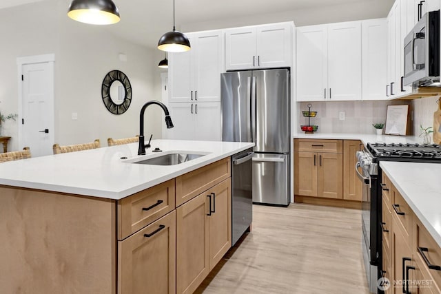 kitchen featuring sink, a center island with sink, pendant lighting, stainless steel appliances, and white cabinets