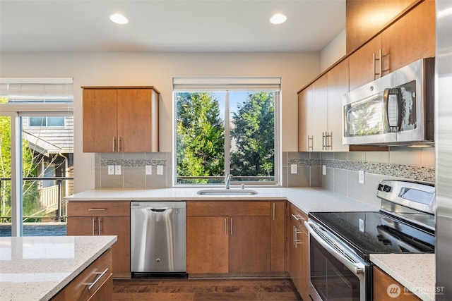 kitchen with appliances with stainless steel finishes, sink, decorative backsplash, light stone countertops, and dark wood-type flooring