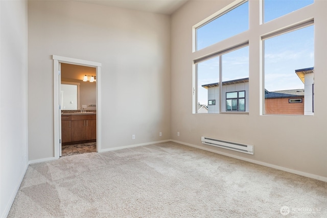 unfurnished room with sink, a towering ceiling, light colored carpet, and baseboard heating