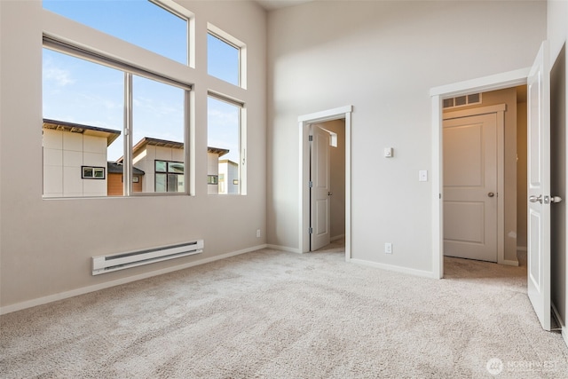 carpeted empty room featuring a baseboard radiator and a high ceiling