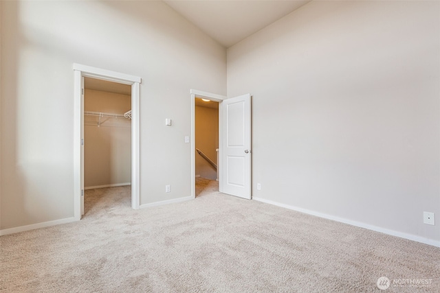 unfurnished bedroom featuring a walk in closet, light colored carpet, a closet, and a high ceiling