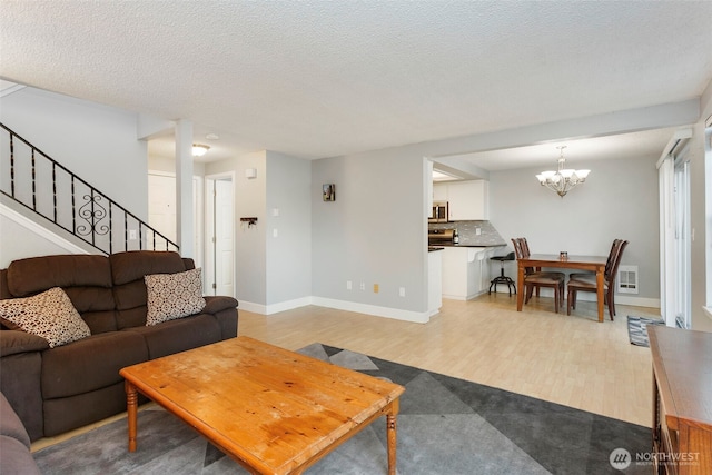 living room with a chandelier, a textured ceiling, and light wood-type flooring