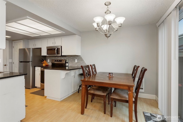 dining space with a textured ceiling, a notable chandelier, and light hardwood / wood-style floors