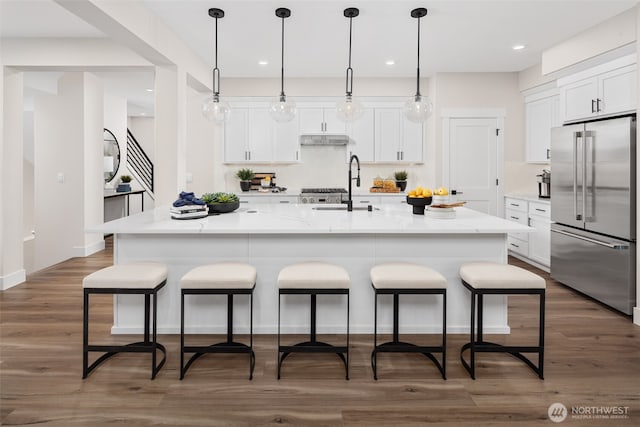 kitchen featuring sink, high end refrigerator, a large island with sink, pendant lighting, and white cabinets