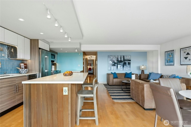 kitchen featuring a center island, a kitchen breakfast bar, light hardwood / wood-style floors, white cabinets, and stainless steel refrigerator