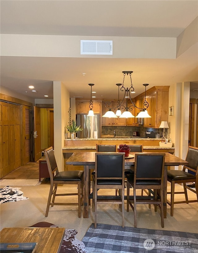 bar with hanging light fixtures, decorative backsplash, and stainless steel fridge