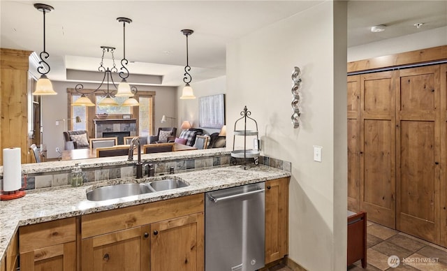 kitchen featuring sink, light stone counters, stainless steel dishwasher, pendant lighting, and a tiled fireplace