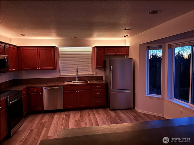 kitchen with appliances with stainless steel finishes, sink, a textured ceiling, and light hardwood / wood-style flooring