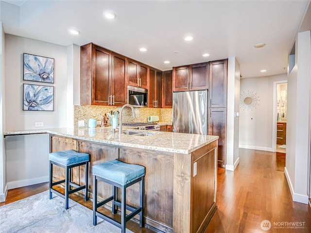 kitchen with light stone counters, a peninsula, a sink, appliances with stainless steel finishes, and tasteful backsplash