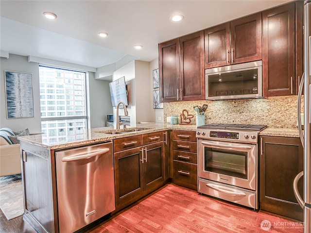 kitchen featuring stainless steel appliances, a peninsula, a sink, light wood-style floors, and decorative backsplash