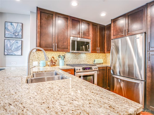 kitchen featuring backsplash, light stone counters, stainless steel appliances, and a sink