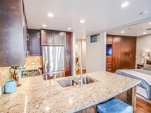 kitchen with a peninsula, a sink, backsplash, light stone countertops, and stainless steel fridge