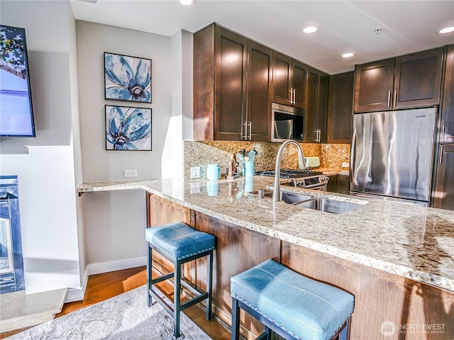 kitchen featuring tasteful backsplash, wood finished floors, light stone countertops, stainless steel appliances, and dark brown cabinets