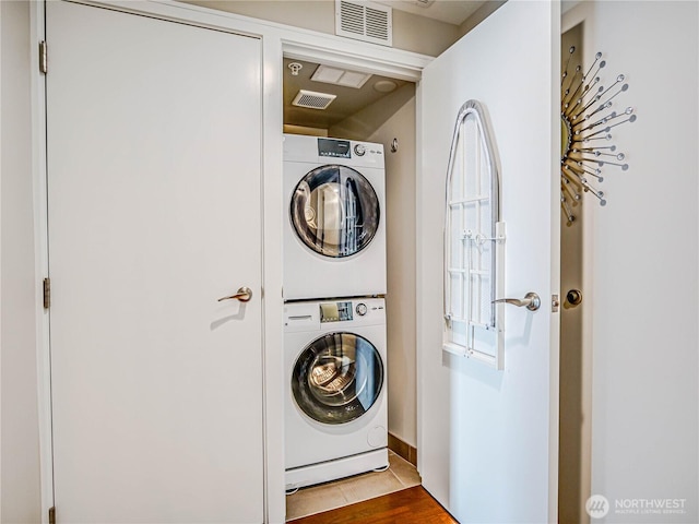 clothes washing area with laundry area, wood finished floors, visible vents, and stacked washer / drying machine