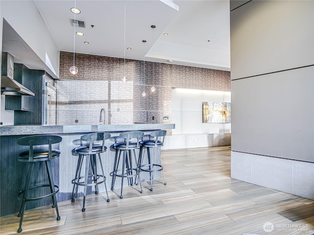 kitchen featuring visible vents, hanging light fixtures, light countertops, a kitchen bar, and a sink