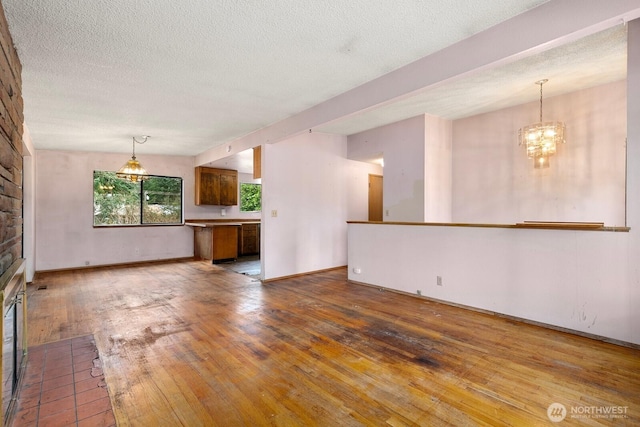 unfurnished living room with a chandelier, a textured ceiling, baseboards, and hardwood / wood-style floors