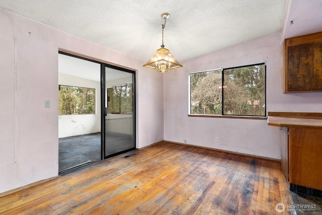 unfurnished dining area with light wood-style flooring, a notable chandelier, visible vents, and a textured ceiling