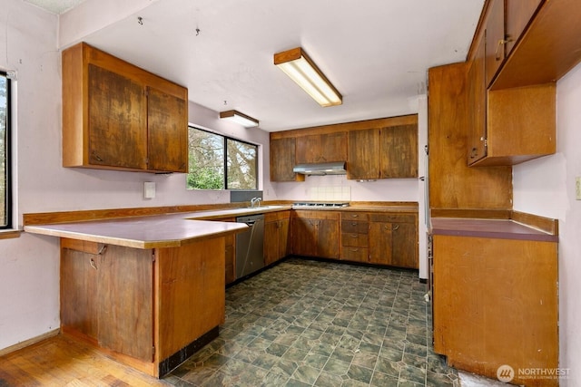 kitchen with under cabinet range hood, brown cabinets, stainless steel dishwasher, and a peninsula