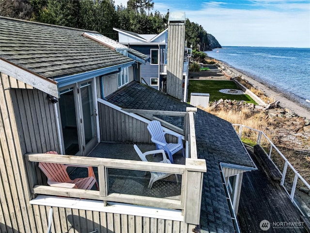 view of side of property with a water view, a beach view, and roof with shingles