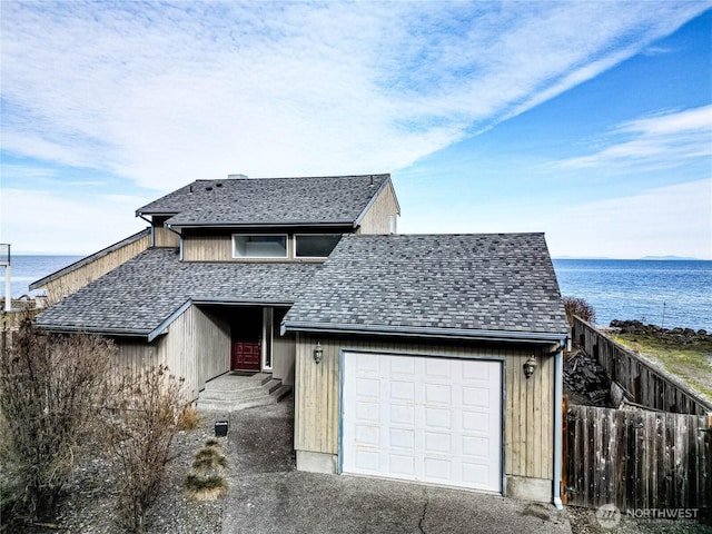 view of front of house with a shingled roof, a water view, fence, and a garage