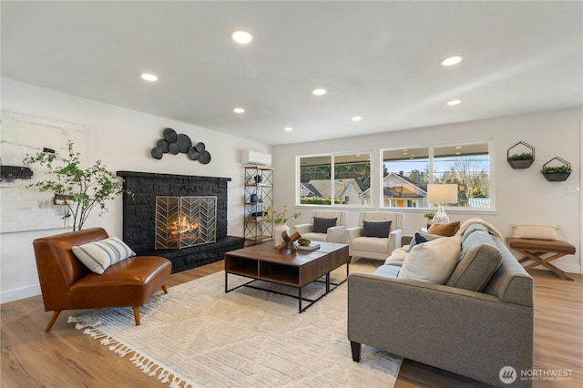 living room featuring a fireplace, a wall unit AC, and light hardwood / wood-style floors