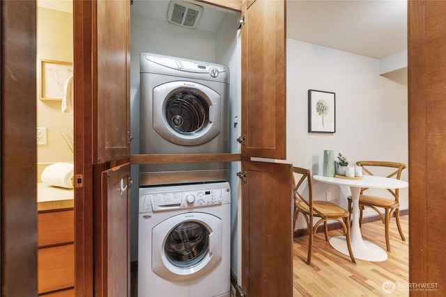 laundry room with stacked washer and dryer and light hardwood / wood-style floors