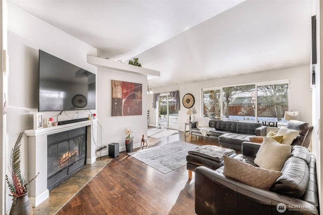 living room featuring lofted ceiling, a fireplace, baseboards, and wood finished floors