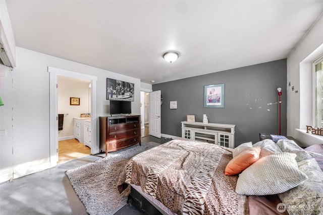 bedroom with concrete flooring, ensuite bath, and baseboards