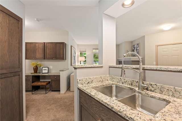 kitchen with light stone countertops, sink, light colored carpet, and dark brown cabinetry