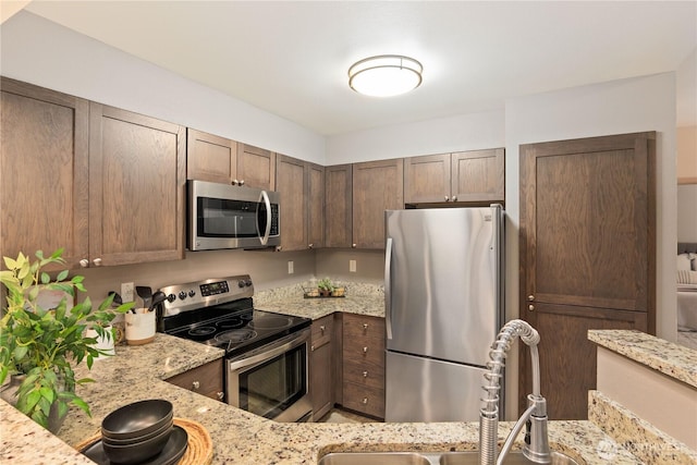 kitchen with light stone countertops, appliances with stainless steel finishes, sink, and dark brown cabinetry