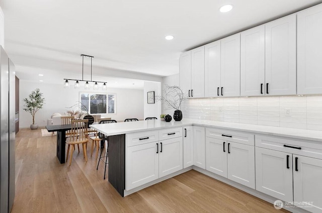 kitchen with hanging light fixtures, white cabinets, light hardwood / wood-style floors, and kitchen peninsula