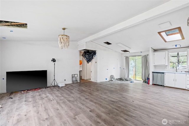 unfurnished living room with vaulted ceiling with skylight, a sink, plenty of natural light, and light wood finished floors