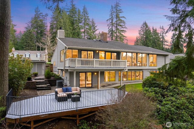 back of house at dusk with a balcony, central AC unit, an outdoor living space, a chimney, and an outdoor structure