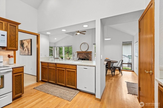 kitchen featuring light wood-type flooring, brown cabinets, a sink, white appliances, and light countertops