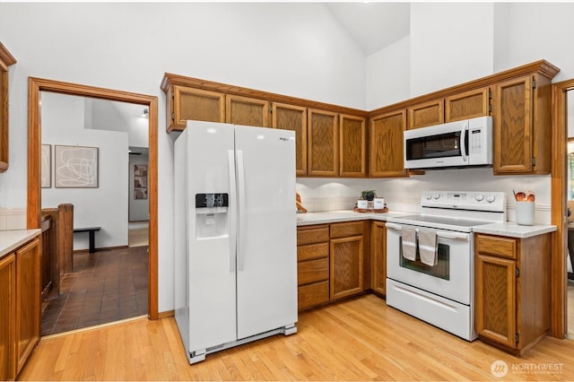 kitchen featuring light wood-type flooring, high vaulted ceiling, white appliances, brown cabinetry, and light countertops