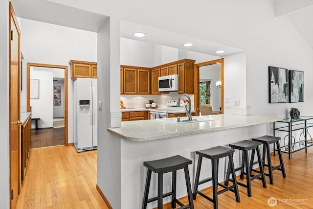 kitchen with light wood-type flooring, a sink, a kitchen breakfast bar, white appliances, and a peninsula