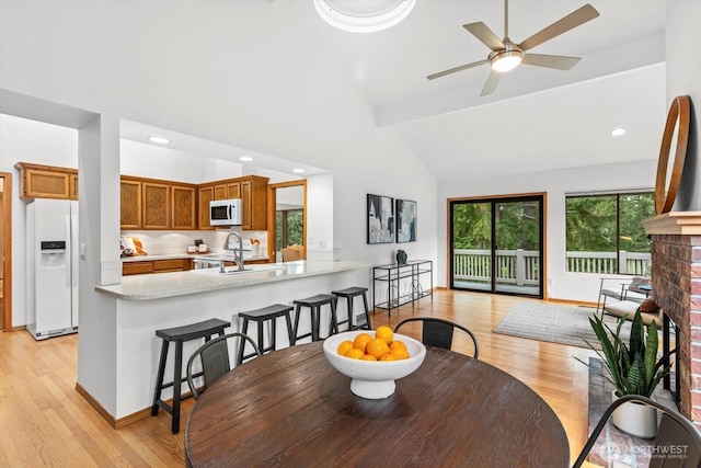 dining room with baseboards, light wood-style floors, ceiling fan, and high vaulted ceiling