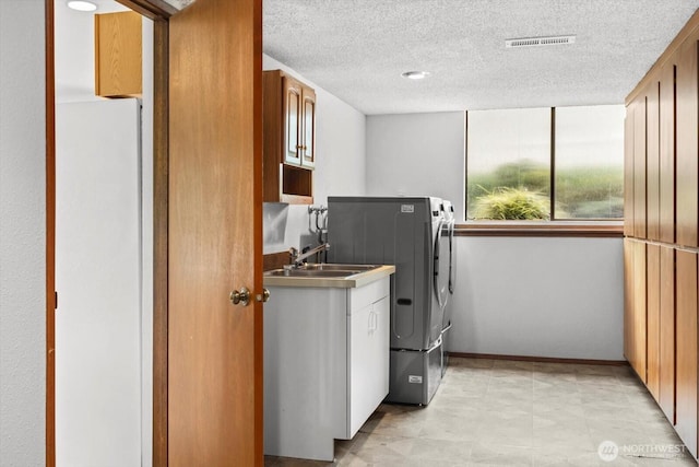 laundry area with visible vents, cabinet space, a sink, a textured ceiling, and washing machine and dryer