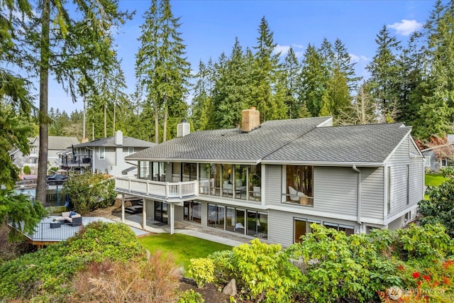 rear view of house featuring a patio, a chimney, a balcony, and roof with shingles