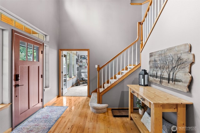 foyer entrance featuring light wood-style flooring, stairway, a towering ceiling, and baseboards