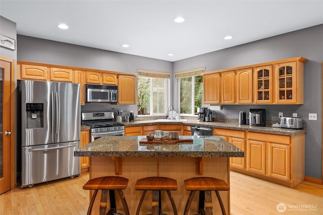 kitchen with a center island, a breakfast bar, light wood finished floors, stainless steel appliances, and glass insert cabinets