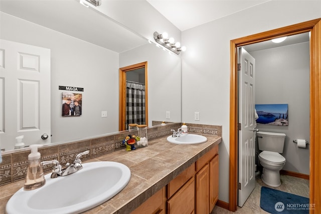 bathroom with toilet, double vanity, baseboards, and a sink