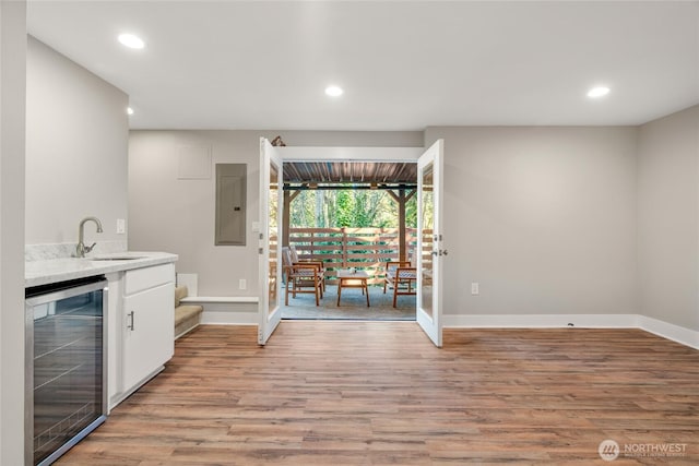 interior space with wine cooler, sink, light wood-type flooring, electric panel, and white cabinets