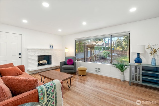 living area with recessed lighting, a brick fireplace, baseboards, and light wood finished floors