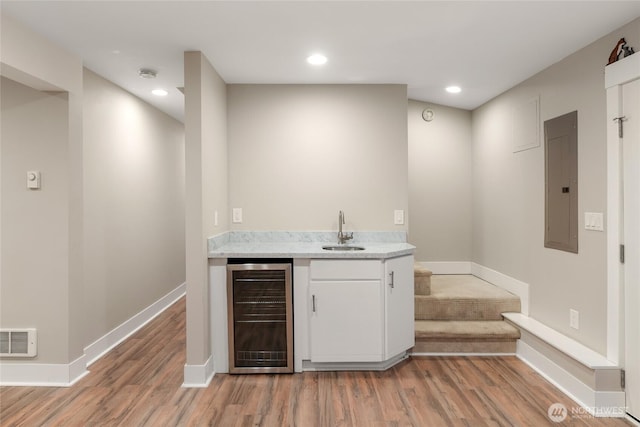 bar featuring sink, light hardwood / wood-style flooring, white cabinetry, electric panel, and beverage cooler