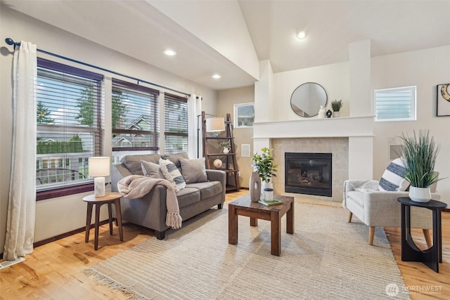 living room with visible vents, vaulted ceiling, recessed lighting, a tile fireplace, and light wood-style floors