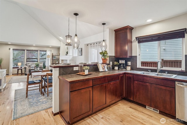 kitchen with a sink, vaulted ceiling, stainless steel dishwasher, dark countertops, and light wood-type flooring