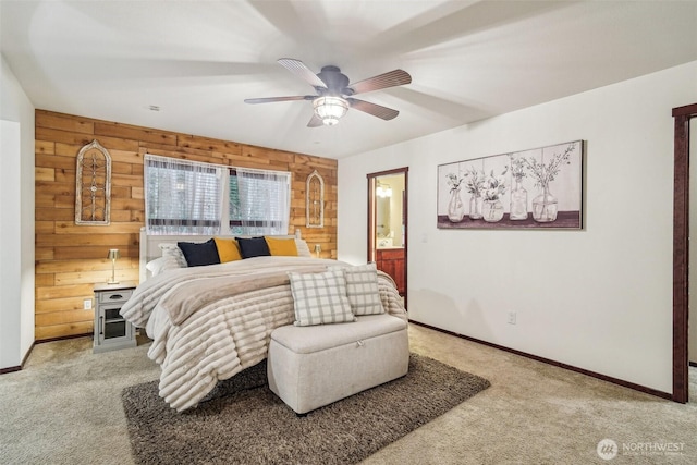 carpeted bedroom with connected bathroom, baseboards, wooden walls, and a ceiling fan