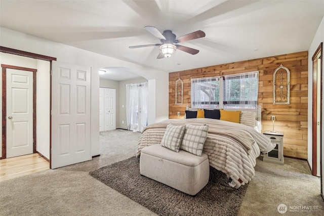 bedroom featuring arched walkways, wooden walls, and light carpet