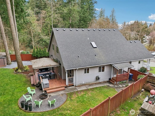 back of house featuring a wooden deck, a yard, a fenced backyard, and an outdoor fire pit